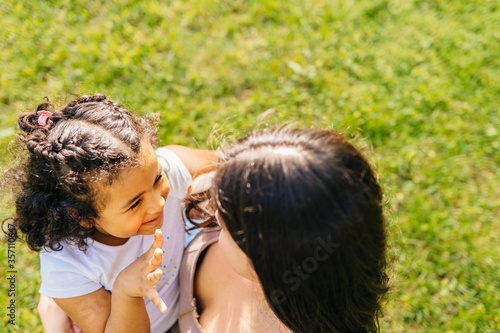 Lovely ecuadorian woman hugging, walking, caressing and caring her mixed race dark skinned daughter in summer vacation, outdoor at city street.