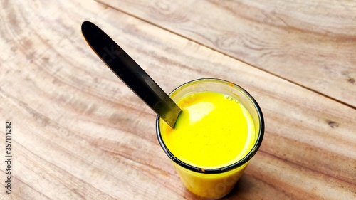 Turmeric mixed milk glass with spoon on the wood table