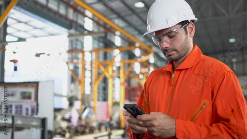 Technician in Hard Hat Using Mobile Phone in Industrial Environment.