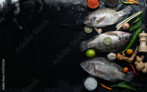 Delicious fresh fish on dark background. Fish with aromatic herbs, spices and vegetables - healthy food, diet or cooking concept