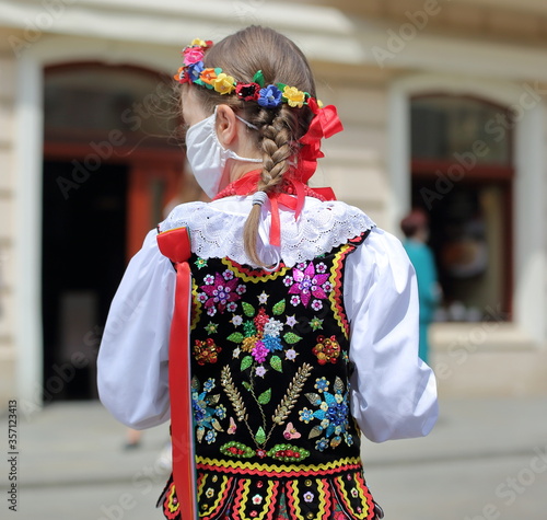 girl in traditional folk costume from Krakow region, wears mask on her face, in the street