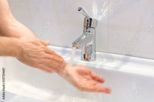 closeup of young caucasian man washing his hands with soap in the sink of bathroom Personal hygiene, protection against viruses and bacteria concept