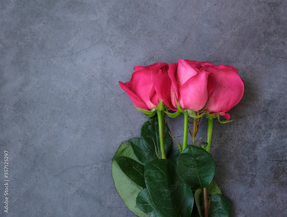 A bouquet of three red roses with green foliage on a gray concrete background