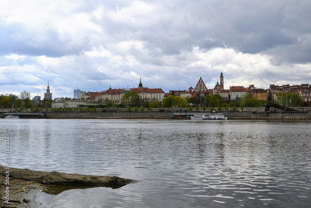 Scenic view of the Old Town - historic quarter of Warsaw with Royal Castle and red roof tenements seen from the Vistula river side. Cloudy day in Warsaw, Poland
