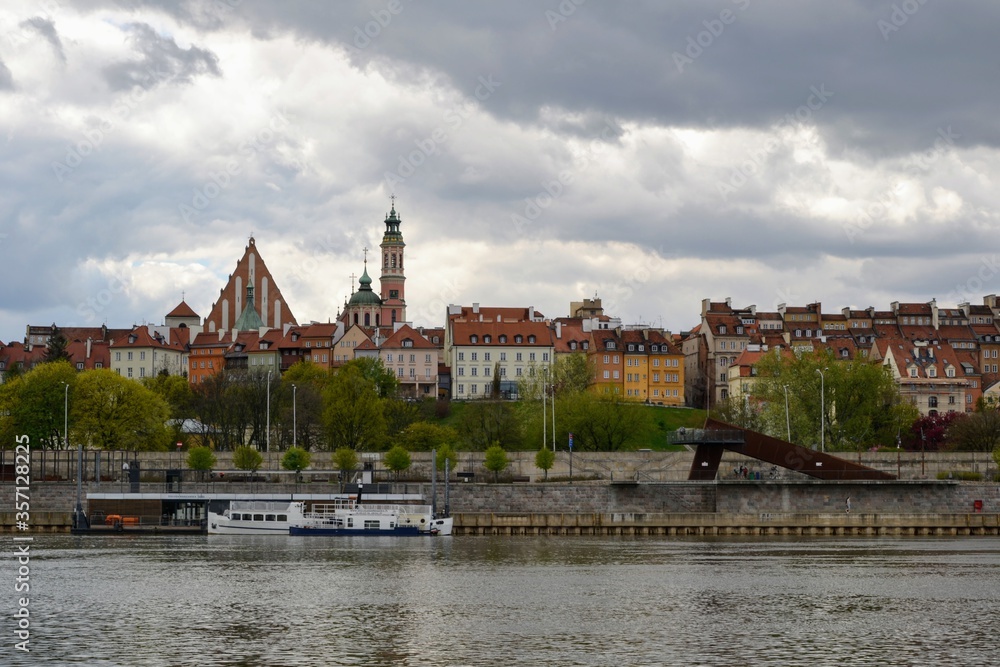 Scenic view of the Old Town - historic quarter of Warsaw with Royal Castle and red roof tenements seen from the Vistula river side. Cloudy day in Warsaw, Poland