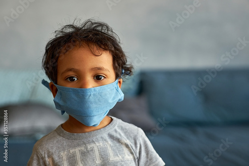 Portrait of a cute african american boy in mask at home - contagion of the Novel Coronavirus 2019- ncov - virus incubation isolation
