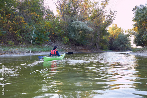 Woman rowing in a green kayak in early autumn along the trees at the bank of Danube river
