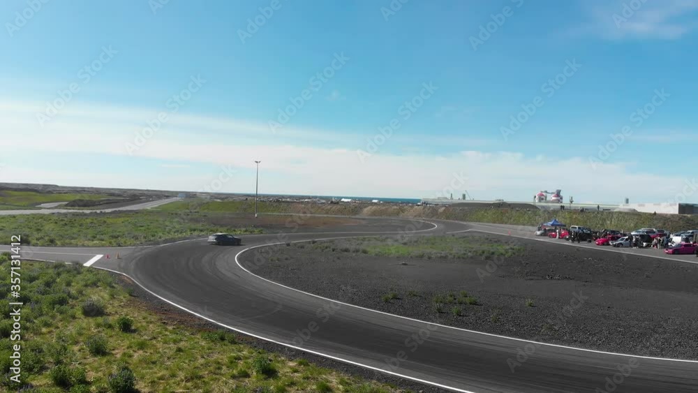Dramatic tracking view of fast blue sedan car smoking tires drifting through hairpin corners on asphalt road, aerial approach Dramatic tracking view of fast blue sedan car smoking tires drifting through hairpin corners on asphalt road, aerial approach
