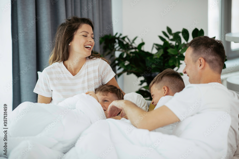 Young family enjoying in bed. Happy parents with sons relaxing in bed. Young family enjoying in bed. Happy parents with sons relaxing in bed.