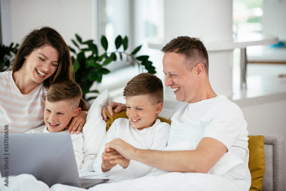 Fototapeta premium Young family watching movie on lap top. Beautiful parents with kids enjoying at home.