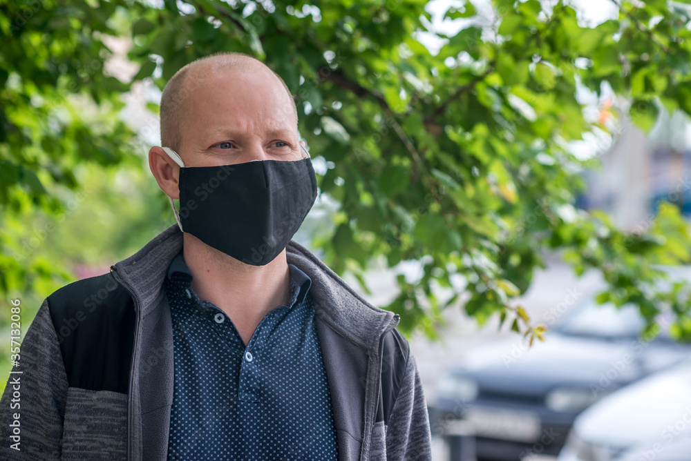 A Caucasian adult man in black protective mask is walking one along empty street and talking on phone. Safe behavior during quarantine and coronavirus pandemic. The new normal and modern reality. A Caucasian adult man in black protective mask is walking one along empty street and talking on phone. Safe behavior during quarantine and coronavirus pandemic. The new normal and modern reality.