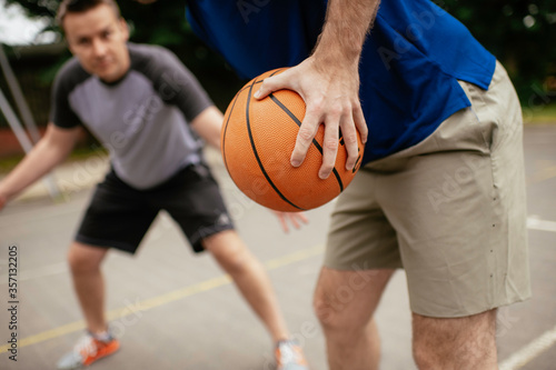 Close up of hands holding ball. Friends playing basketball in the park. © JustLife