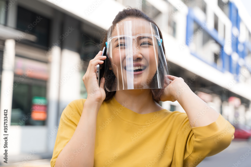 Asian woman is holding a phone outside, wearing a mask or face shield to protect against germs and viruses. Dust prevention and prevention of toxic fumes