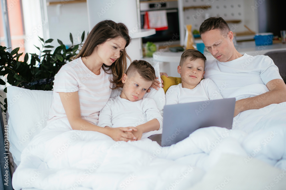 Fototapeta premium Beautiful parents with kids enjoying at home. Young family watching movie on lap top.