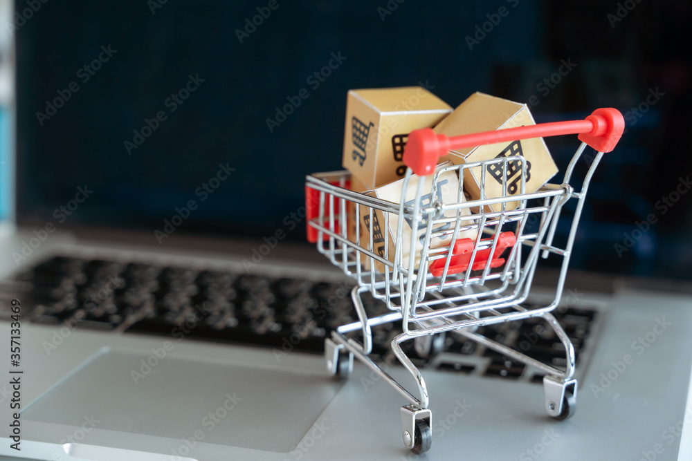 Online shopping / ecommerce and delivery service concept : Paper cartons with a shopping cart on a laptop keyboard, depicts customers order things from retailer sites via the internet.