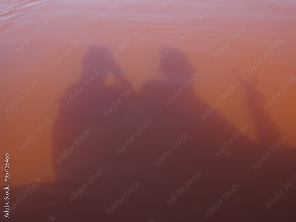 Shadows of people reflected in a slightly reddish-pink lake, Lac Rose, Dakar, Senegal