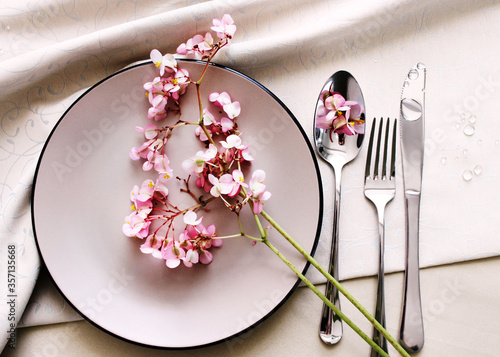 plate and cutlery on the table, top view. pink begonia flowers as a table setting. interior details, festive table setting.