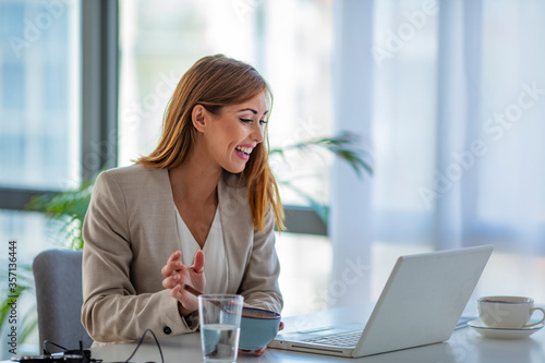 Beautiful young woman sitting at the desk in an office and eating lunch, using laptop at the same time. Business woman eating lunch at her workplace looking at the laptop screen.