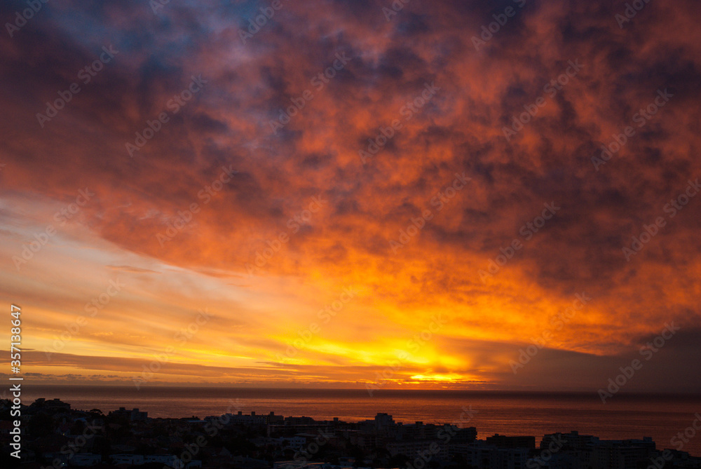Beautiful dramatic sunset clouds in the sky over the sea and silhouette of the city Cape Town, South Africa. Bright Colors Of Sunset.