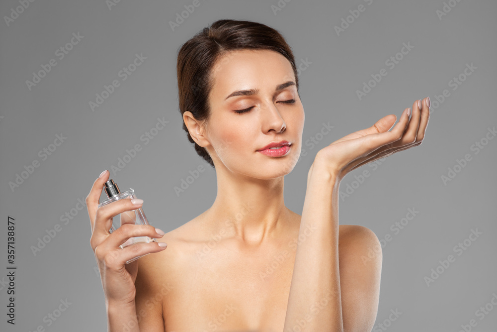 perfumery, beauty and luxury concept - happy young woman smelling perfume from her wrist over grey background perfumery, beauty and luxury concept - happy young woman smelling perfume from her wrist over grey background