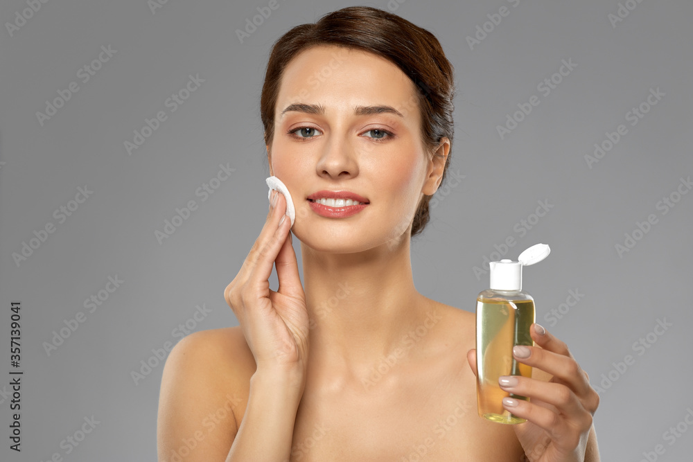 beauty, skin care and people concept - smiling young woman with toner or cleanser and cotton pad cleansing face over grey background beauty, skin care and people concept - smiling young woman with toner or cleanser and cotton pad cleansing face over grey background