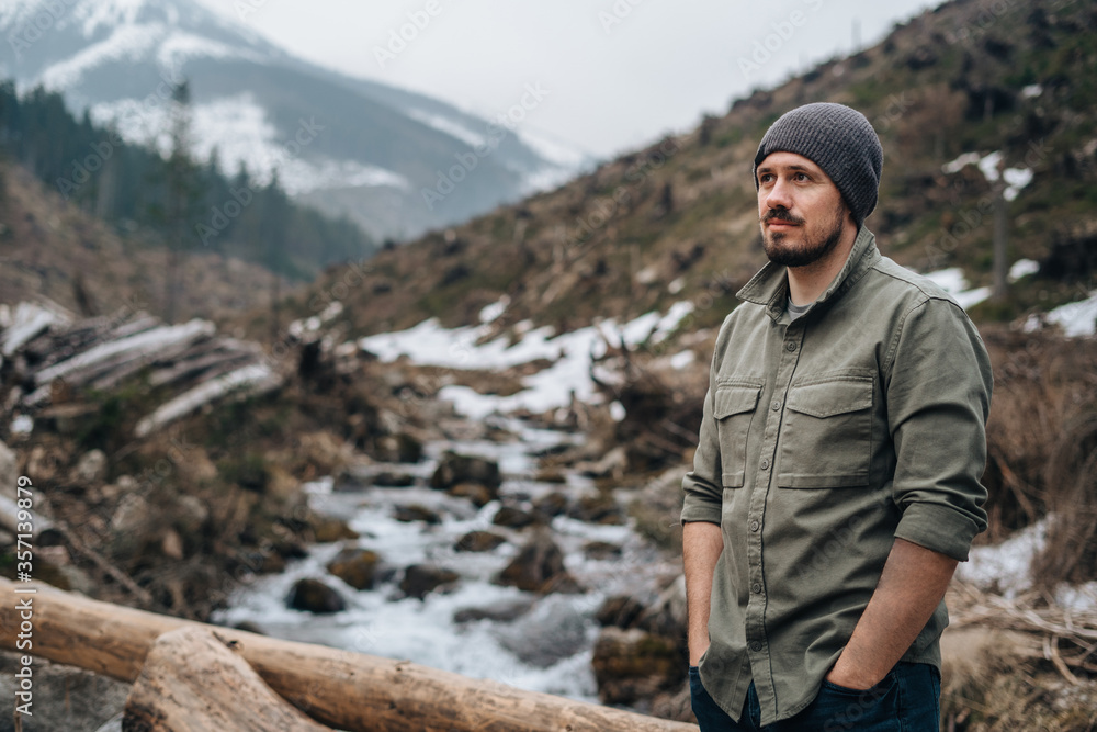 guy with a beard alone on a walk in the woods in a mountainous area. guy looks at the mountains. life in the woods outside the city
