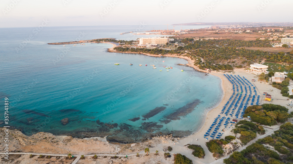 Aerial bird's eye view of Landa beach, Ayia Napa, Famagusta, Cyprus. Landmark tourist attraction golden sand bay at sunrise with boats anchored between Makronissos and nissi in Agia Napa, from above. 