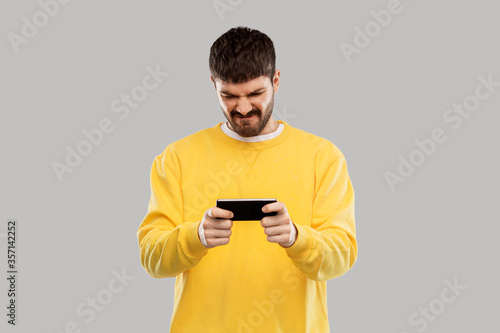 Fotografi technology, communication and people concept - displeased young man playing game