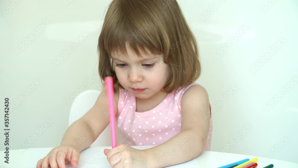 Close up of little girl sitting at table at home. and carefully draws with pink pencil on paper. Education concept. Children's creativity. Close up of little girl sitting at table at home. and carefully draws with pink pencil on paper. Education concept. Children's creativity.
