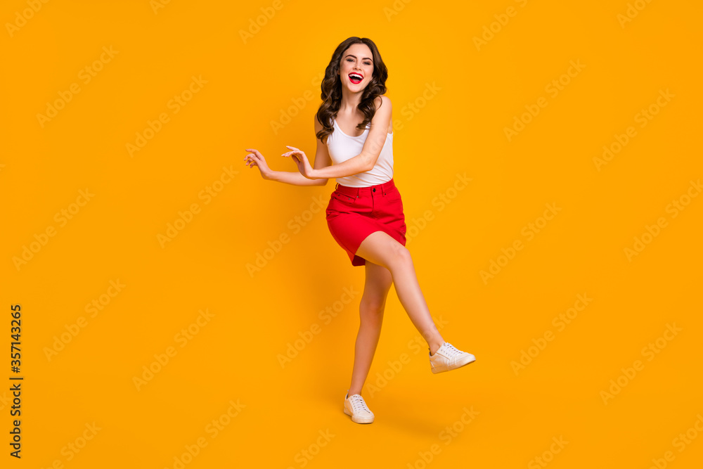 Full length photo of amazing cheerful lady walk down street sunny day good mood raise leg hands laughing wear white casual singlet red mini skirt shoes isolated yellow color background