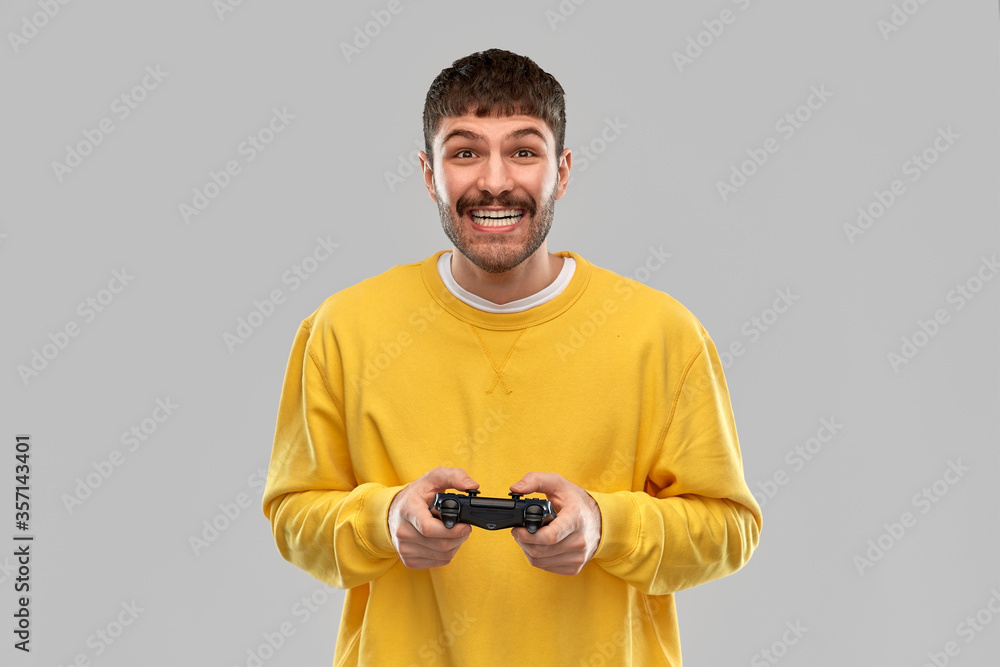 technology, gaming and people concept - happy smiling young man or gamer with gamepad playing video game over grey background technology, gaming and people concept - happy smiling young man or gamer with gamepad playing video game over grey background