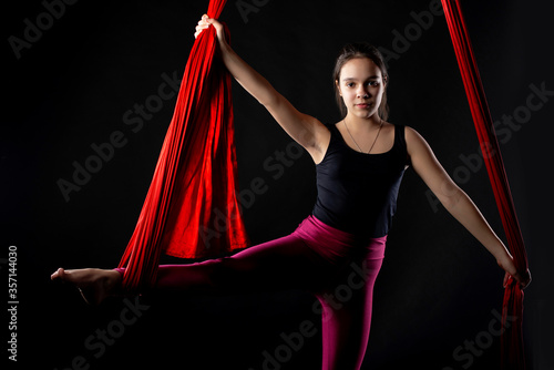 Portrait of purposeful pretty teenage girl with aerial red ribbons on black background before start of gymnastics show. Acrobatics and sports concept for children and adolescents photo