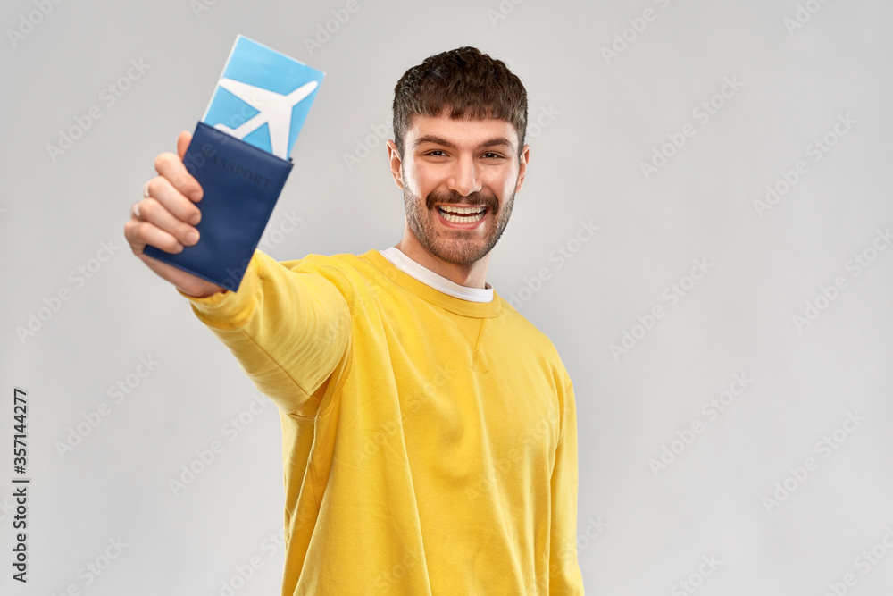 travel, tourism and people concept - smiling young man in yellow sweatshirt with air ticket and passport over grey background travel, tourism and people concept - smiling young man in yellow sweatshirt with air ticket and passport over grey background