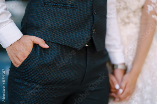 Groom in a navy suit holding his hand in his pocket. Bride is holding his other hand with hers. Fine-art wedding photo in Montenegro, Perast.