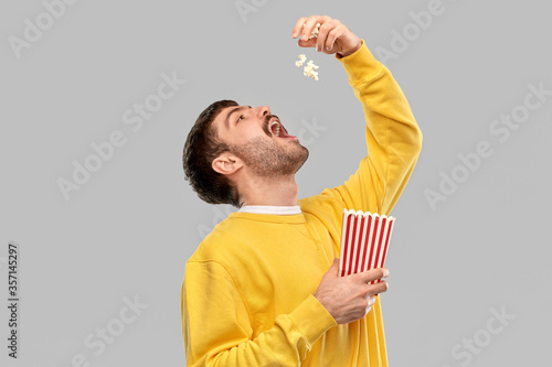 fast food people concept - young man in yellow sweatshirt eating popcorn throwing it to open mouth over grey background