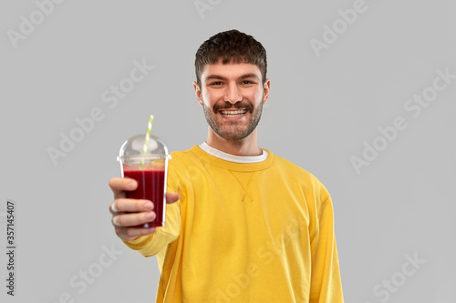 drinks and people concept - happy smiling young man holding tomato juice in takeaway plastic cup with paper straw over grey background