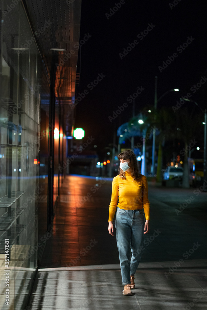 Beautiful young woman with face mask walks looking at empty shelves in shop on city street at night