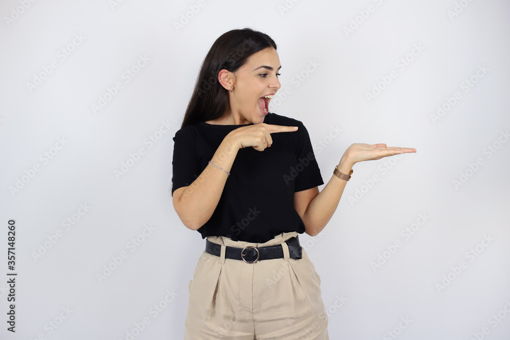 Young beautiful woman standing over white isolated background surprised, smiling and showing something that is on her hand Young beautiful woman standing over white isolated background surprised, smiling and showing something that is on her hand