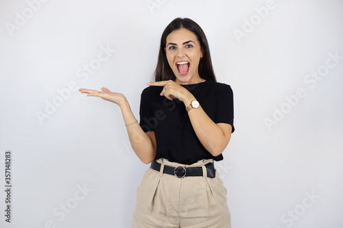 Young beautiful woman standing over white isolated background surprised, smiling and showing something that is on her hand.