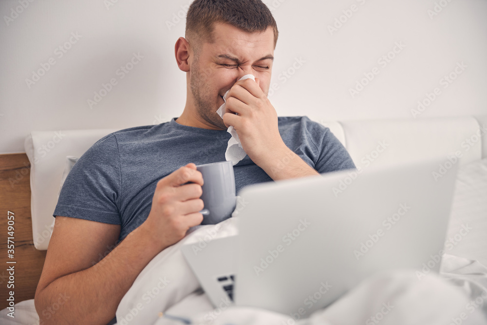 Handsome male is drinking tea and sneezing Handsome male is drinking tea and sneezing
