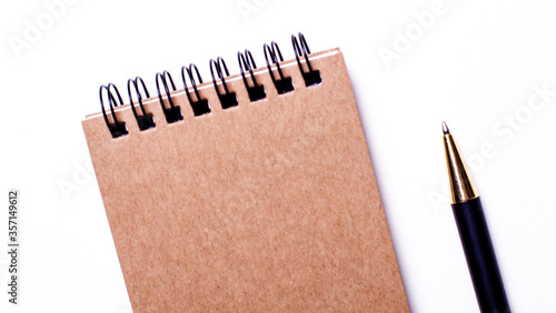 On a white table lies a brown notebook on springs and a black pen. Close up business concept