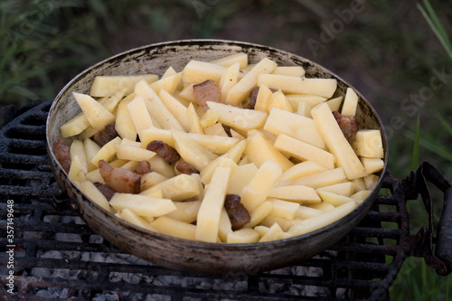 Sliced raw potatoes in a pan over charcoal. Outdoor barbecue. Preparing food