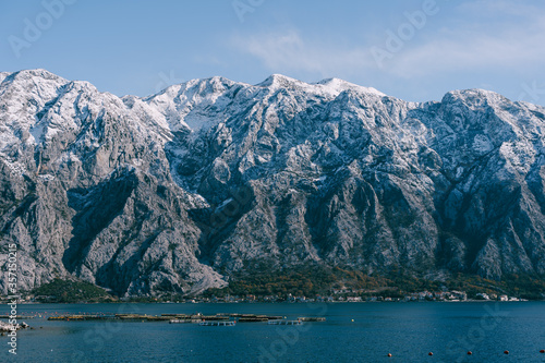 Snow-capped mountain peaks in Kotor Bay, Montenegro, above the city of Dobrota. An assiable and fish farm in the sea.