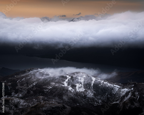 Beautiful landscape view of snowy mountain Ben Nevis with dramatic clouds above the peak during sunrise