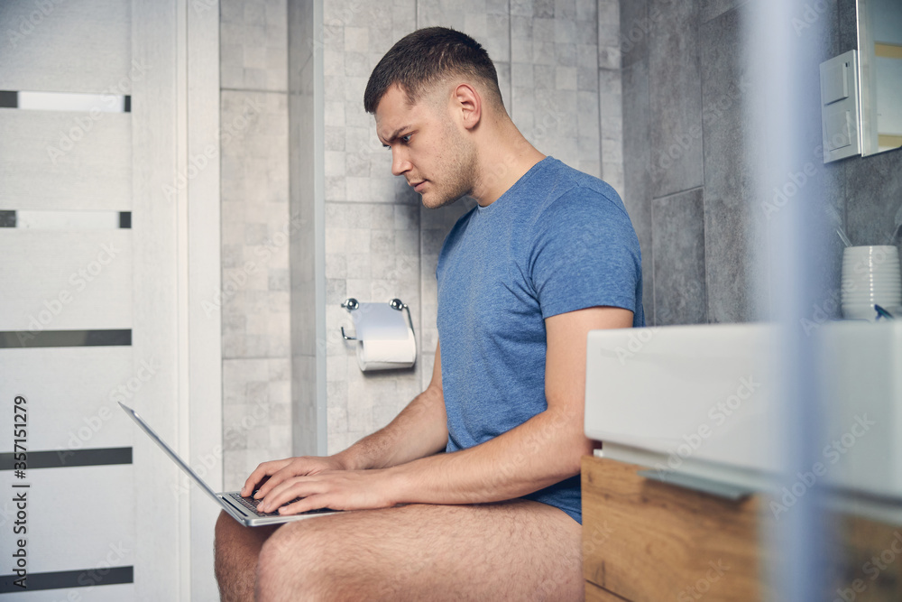 Handsome brunette male without trousers working in bathroom