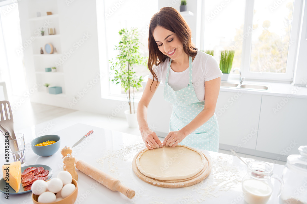 Portrait of positive cheerful girl housewife prepare pizza make crusts on wooden chopping board wear dotted apron in white modern kitchen Portrait of positive cheerful girl housewife prepare pizza make crusts on wooden chopping board wear dotted apron in white modern kitchen