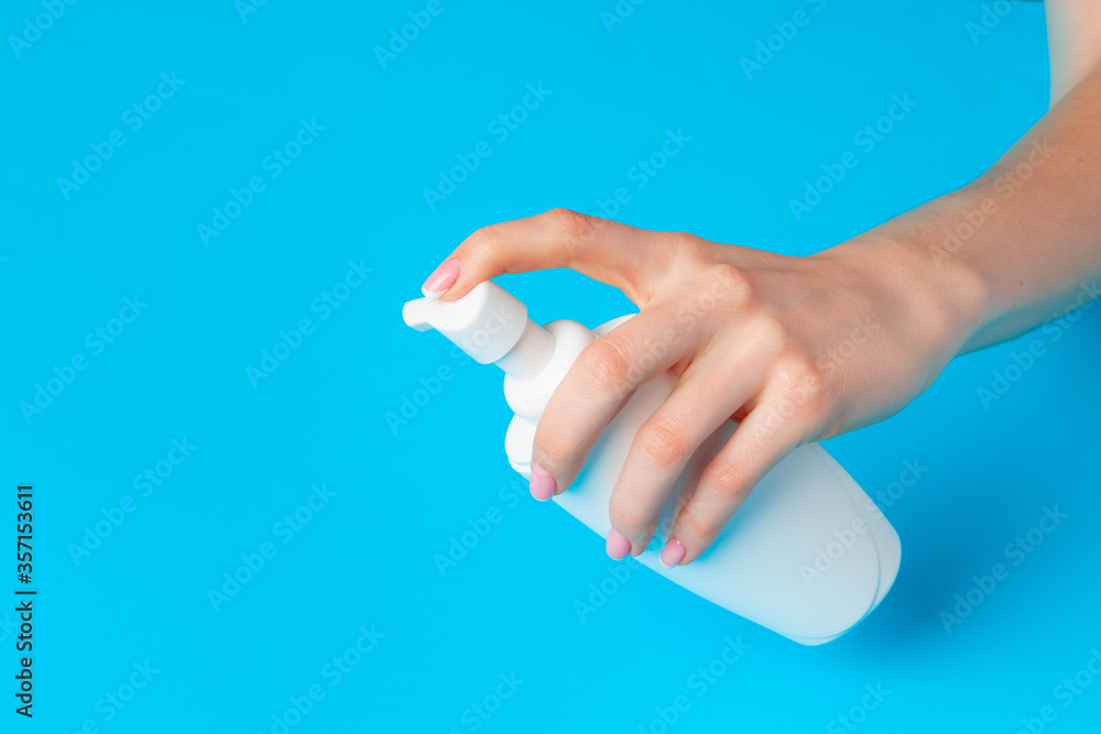 Female hand holding skincare product bottle on blue Female hand holding skincare product bottle on blue