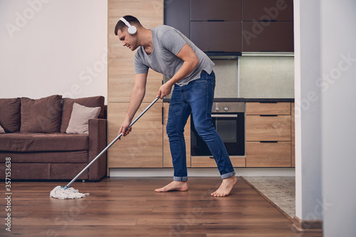 Young sporty male cleaning parquet in living room