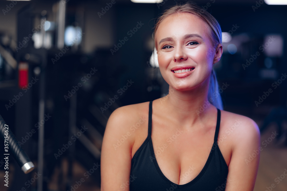 Close up portrait of a young blonde woman in sport bra in a dark gym