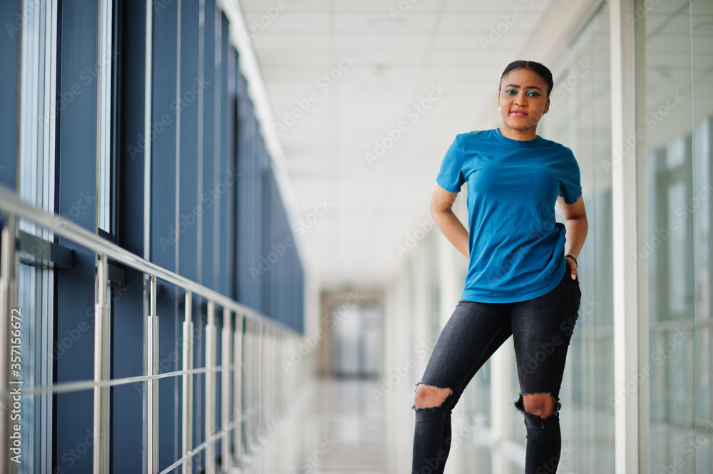 African woman in blue t-shirt posed indoor together. African woman in blue t-shirt posed indoor together.
